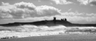 Powerful shot of Dunstanburgh Castle from Embleton beach with surf rolling in on a windy day in summer