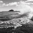 Bamburgh Castle with waves crashing onto rocks in the foreground, Northumberland, Northumbria