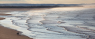 Couple walking at Budle Point, Budle Bay, Northumberland With Ross Links in the distance