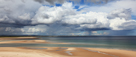 Lindisfarne, Holy Island viewed across Budle Bay, Northumberland with clouds sunlight and rain